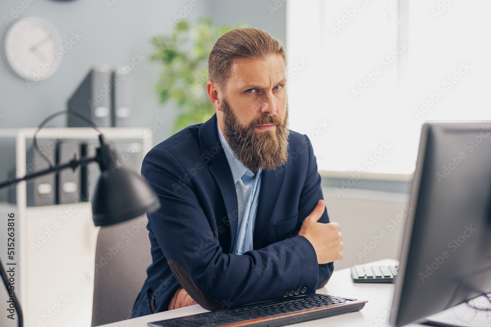 Fototapeta premium Pensive mature man in stylish business wear sitting at desk with modern pc. Successful caucasian male person working at bright office. Career and people concept.