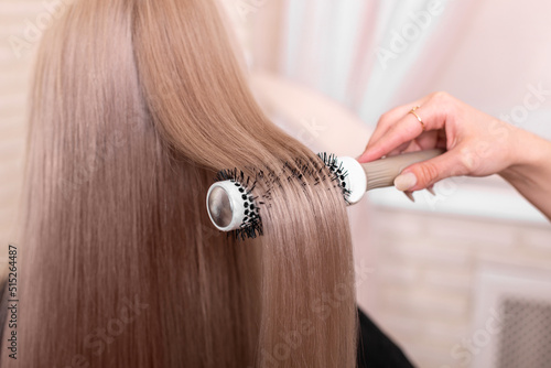 Hairdresser's hand brushing long silver blonde hair in beauty salon