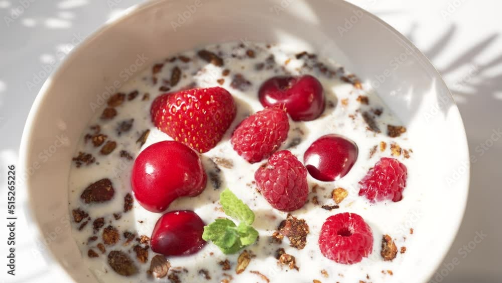 Hand of woman takes cherries and strawberries throwing in bowl on white table. Housewife prepares healthy breakfast in sunny morning closeup Hand of woman takes cherries and strawberries throwing in bowl on white table. Housewife prepares healthy breakfast in sunny morning closeup