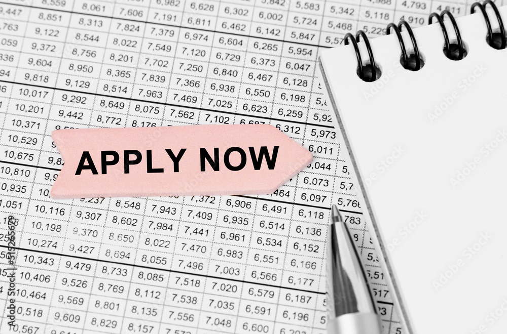 Fototapeta premium On the table among the reports is a notebook, a pen with an arrow with the inscription - APPLY NOW