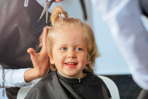 Portrait of a little blond boy smile to hairdresser make haircut