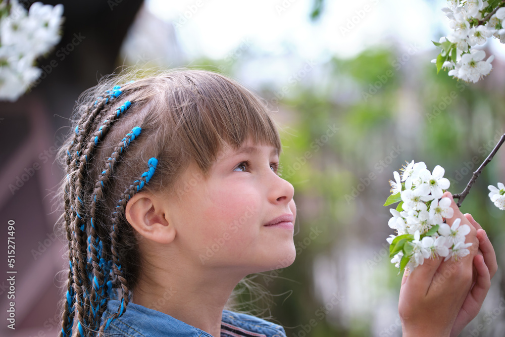 Naklejka premium Happy child girl playing in spring garden enjoying sweet scent of white cherry tree blossoming flowers on sunny day