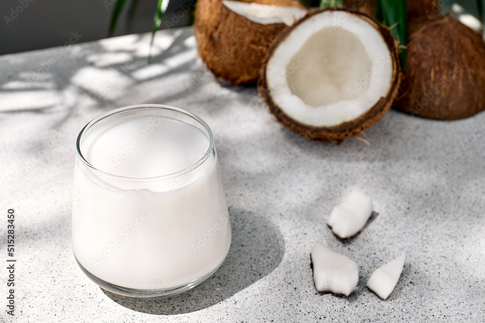 Coconut milk in glass and half of coconut on palm leaf background. Vegetable milk, lactose free non dairy healthy drink. Vegan food. Coconut milk in glass and half of coconut on palm leaf background. Vegetable milk, lactose free non dairy healthy drink. Vegan food.