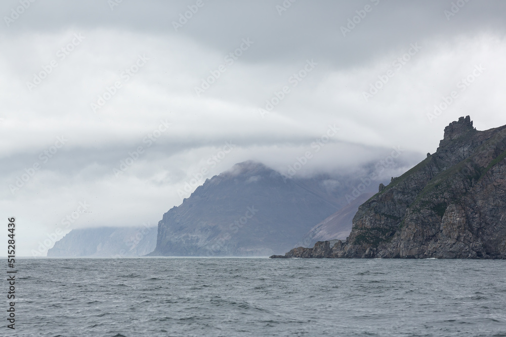 Epic arctic seascape. View of the rocky capes on the coast of the Bering Sea. Low clouds. Harsh northern nature. Majestic rocks. Eastern coast of Chukotka, Russian Far East. Sea cruises to the Arctic.