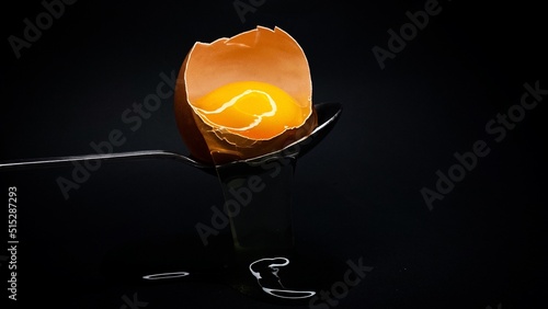 A broken egg on a spoon on a black background. photo