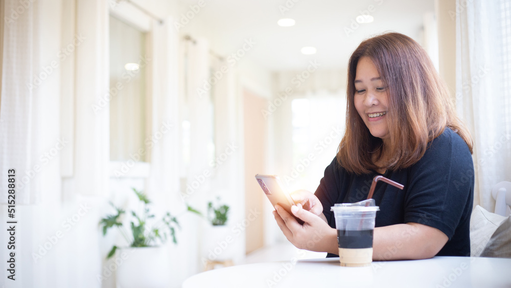 Happy Asian woman holding and using mobile phone in cafe or coffee shop with copy space. Happy Asian woman holding and using mobile phone in cafe or coffee shop with copy space.