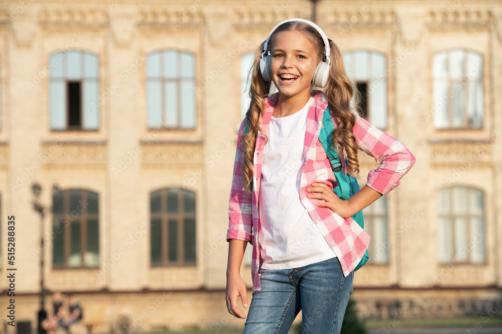 Fototapeta premium Happy teen girl listening to music in school yard outdoors, copy space
