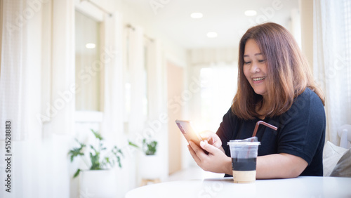 Happy Asian woman holding and using mobile phone in cafe or coffee shop with copy space.