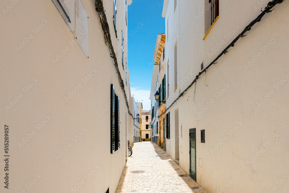 A narrow whitewashed alley under a blue summer sky in the historic medieval center of Ciutadella de Menorca, Spain, on the Balearic island of Menorca in the Mediterranean Sea