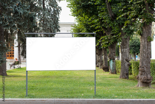 Billboard in the park against the background of large old trees.