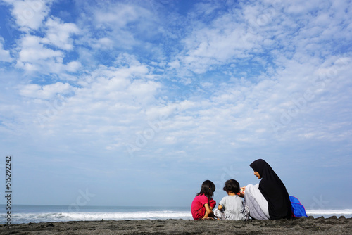 A hijabi mother plays in the sand with her two daughters on the beach