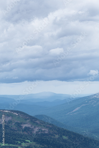 Gentle hills in gray haze on horizon. Rock ridge under sunset sky. Clouds gathered on mountain valley. Mystery of Future Weather Uncertainty