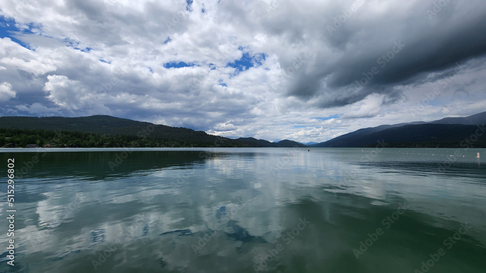 Whitefish Lake in Flathead County, Montana under dramatic summer cloudscape reflected in calm water of lake.