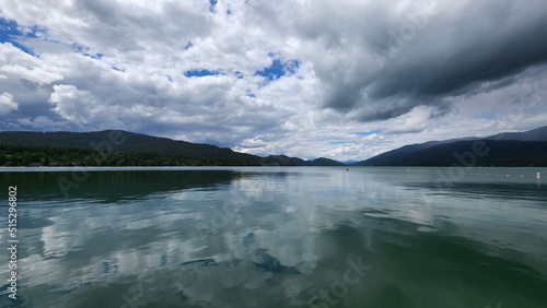 Whitefish Lake in Flathead County, Montana under dramatic summer cloudscape reflected in calm water of lake. photo