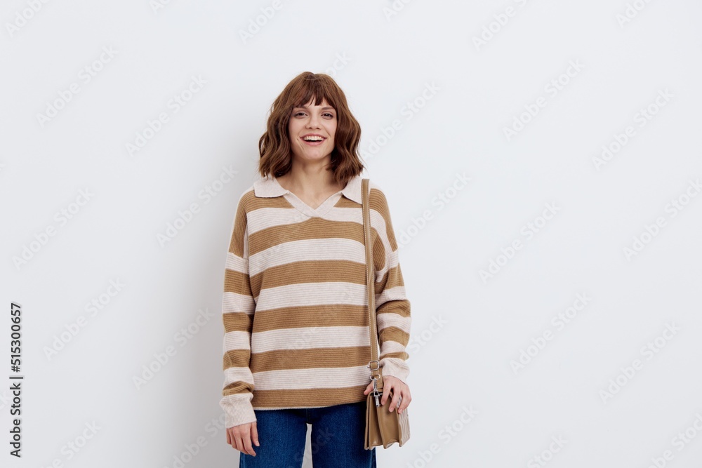 sweet woman stands in a stylish striped sweater and jeans with a beige bag over her shoulder and looks at the camera with a pleasant smile on her face. Horizontal photo with an empty space sweet woman stands in a stylish striped sweater and jeans with a beige bag over her shoulder and looks at the camera with a pleasant smile on her face. Horizontal photo with an empty space
