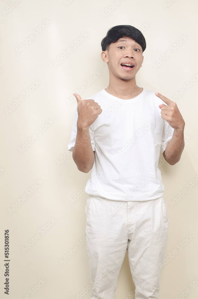 Portrait of surprised Asian man in white coat smiling and looking at camera pointing with two hands and fingers to the side Portrait of surprised Asian man in white coat smiling and looking at camera pointing with two hands and fingers to the side