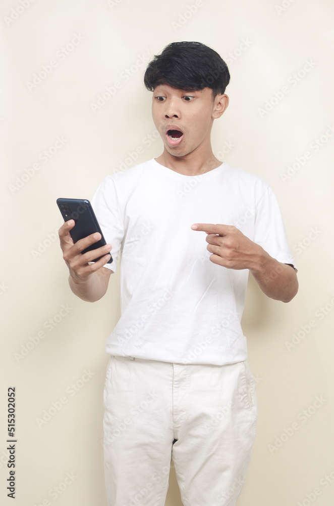 Handsome Asian guy in studio looks surprised at screen of mobile phone