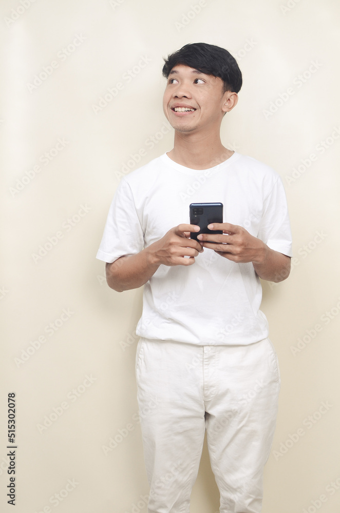 Asian man holding cell phone with smiling face looking sideways Asian man holding cell phone with smiling face looking sideways