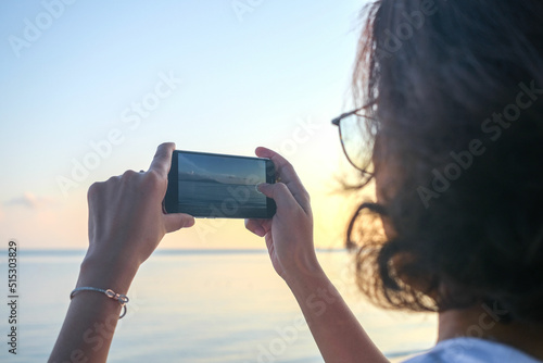 Woman taking pictures of beach, sea and resort at sunrise He used his phone to take high-angle shots. Travel concept and technology © Photo Sesaon