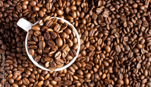 Roasted coffee beans in a white mug on a background of coffee beans.