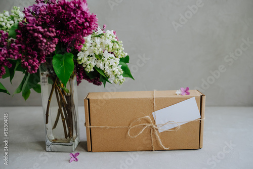 Craft box tied with twine on a bow. Delivery of goods to the door. The package is on a gray background. A bouquet of beautiful and fragrant lilac. Flowers in a vase.