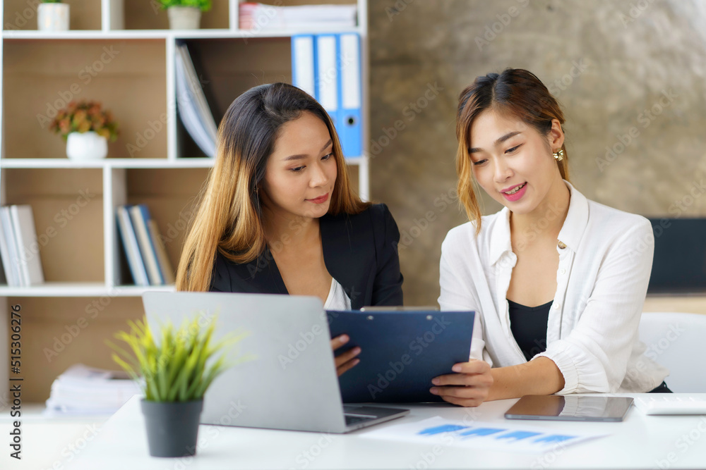 Two Asian business women discuss working together in the office. Two Asian business women discuss working together in the office.