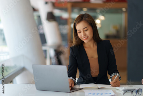 Asian businesswoman sitting happily working on her laptop in the office.