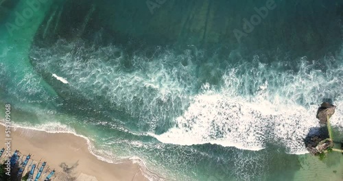 Aerial top down shot of white sandy SIUNG BEACH with crashing waves ending at shore in sunlight - YOGYAKARTA, INDONESIA photo