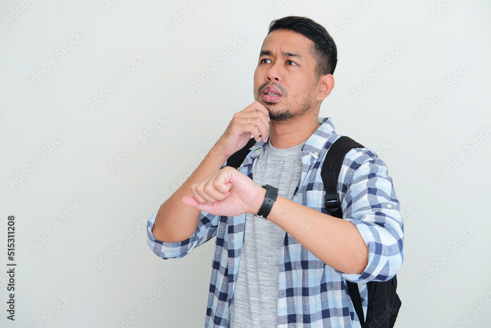Adult Asian man wearing backpack waiting for someone to pick him up with unsure expression Adult Asian man wearing backpack waiting for someone to pick him up with unsure expression