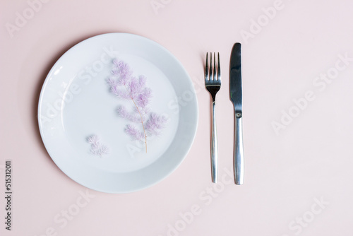 Diet concept with purple flowers over the white plate with fork and knife over the pink background. 