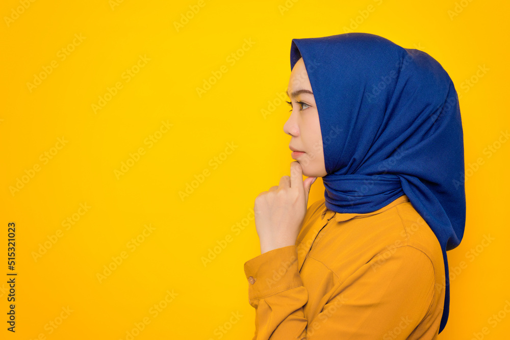 Thoughtful young Asian Muslim woman dressed in orange looking aside at copy space isolated on yellow background Thoughtful young Asian Muslim woman dressed in orange looking aside at copy space isolated on yellow background