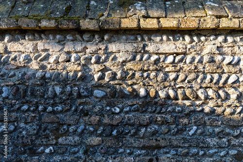 Particolare di antico muro di pietra e mattoni. Muro di recinzione metà illuminato dal sole e metà in ombra.