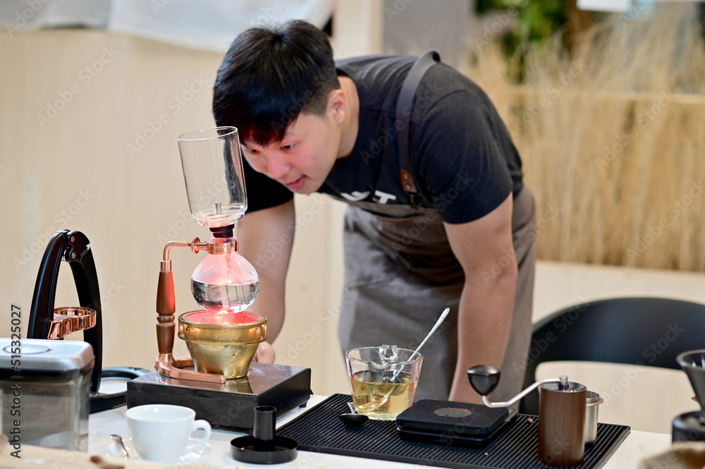 Closeup of Asian Male Barista looking at coffee in brewing machine to wait for the coffee to mix completely will get delicious coffee inside a coffee shop cafe in Thailand. Closeup of Asian Male Barista looking at coffee in brewing machine to wait for the coffee to mix completely will get delicious coffee inside a coffee shop cafe in Thailand.