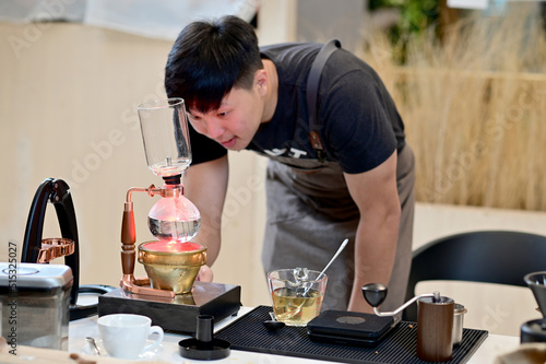 Fototapeta Naklejka Na Ścianę i Meble -  Closeup of Asian Male Barista looking at coffee in brewing machine to wait for the coffee to mix completely will get delicious coffee inside a coffee shop cafe in Thailand.