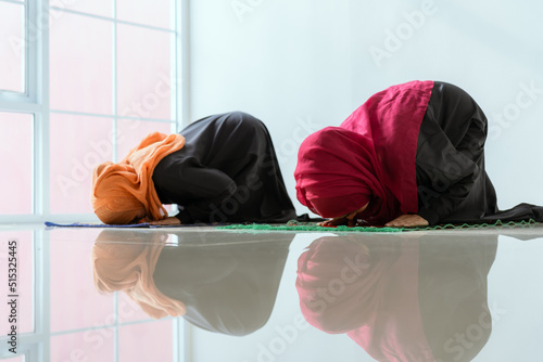 Two young Asian Muslim women in hijab dress sitting and praying together. Idea for religious ritual, education and calm of mind