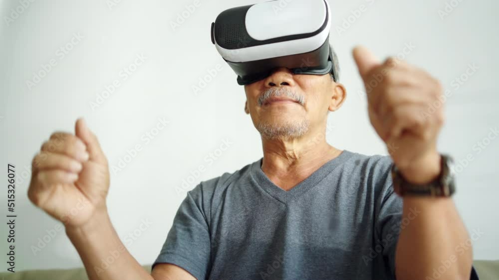 Happy Asian Mature Adult is using VR glasses headset with virtual reality car game at home. Happy Asian Mature Adult is using VR glasses headset with virtual reality car game at home.