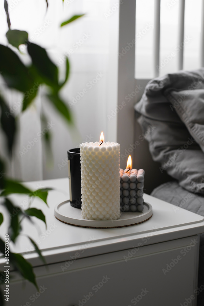 Luxury aroma burning candle in bedroom on bedsite table. Home cozy interior  Photos | Adobe Stock