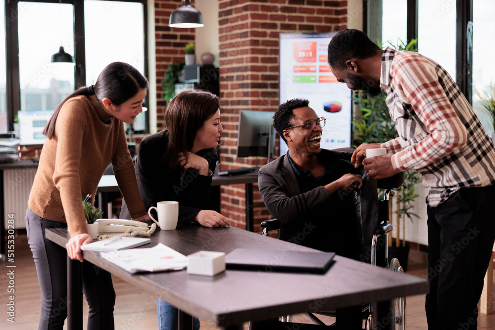 African american man with physical impairment having fun at work, taking break with workmates. Male wheelchair user suffering from chronic disability laughing with business partners. African american man with physical impairment having fun at work, taking break with workmates. Male wheelchair user suffering from chronic disability laughing with business partners.