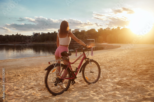Attractive red-haired young woman rides a bicycle on the beach in shorts. Evening. Sunset. sand