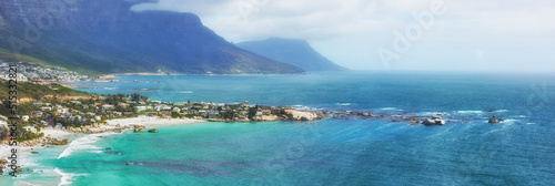 A peaceful view of the Clifton ocean at the Atlantic seaboard with an island and mountains in the background. A city surrounded by blue fresh water and a foggy cloudy sky with copy space.