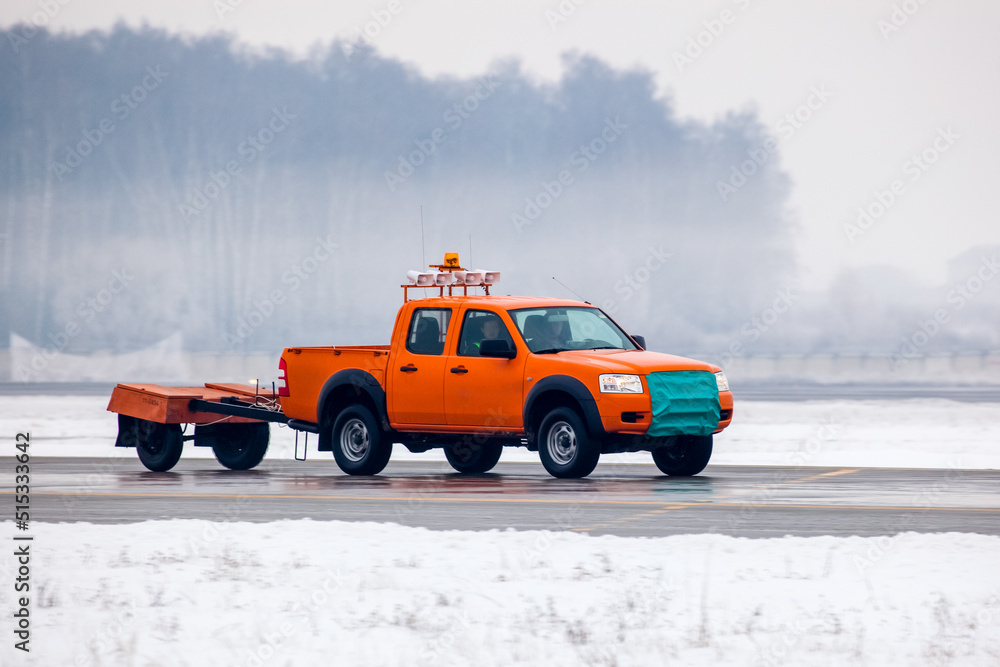 Airport service car on runway on airfield during snowfall Airport service car on runway on airfield during snowfall