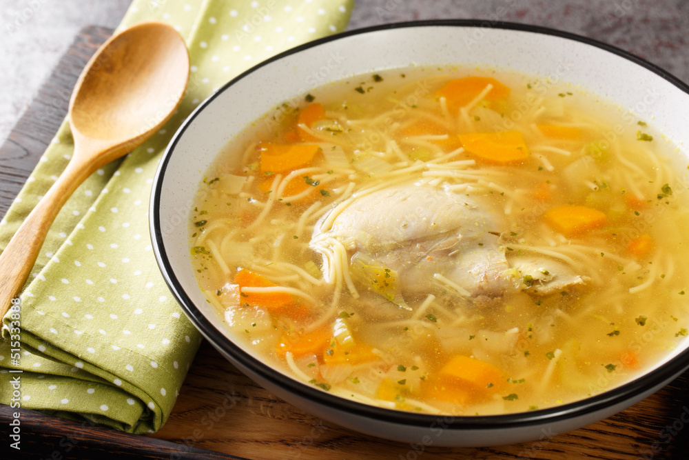 Dietary chicken soup with vermicelli and vegetables close-up in a bowl on a wooden tray on the table. horizontal