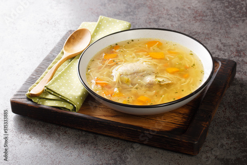 Delicious homemade chicken broth with noodles and vegetables close-up in a plate on a wooden tray. horizontal photo