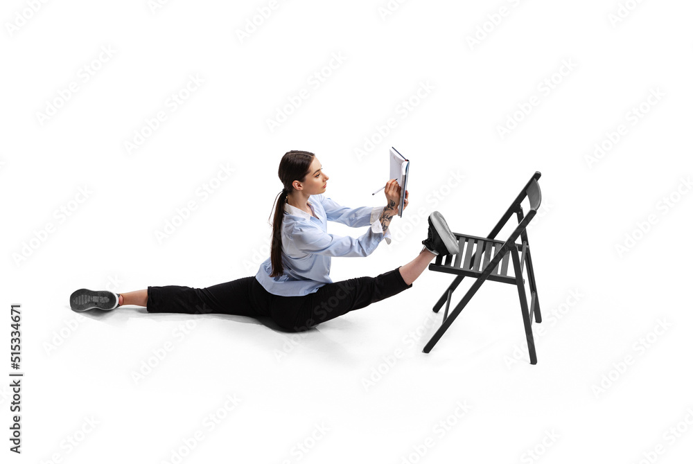 Fototapeta premium Portrait of female office worker sitting on twine and making business notes isolated over white studio background