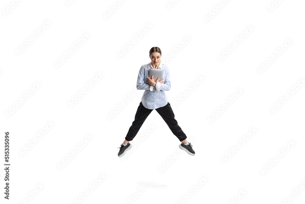 Portrait of young woman, office employee in official outfit jumping with laptop isolated over white studio background