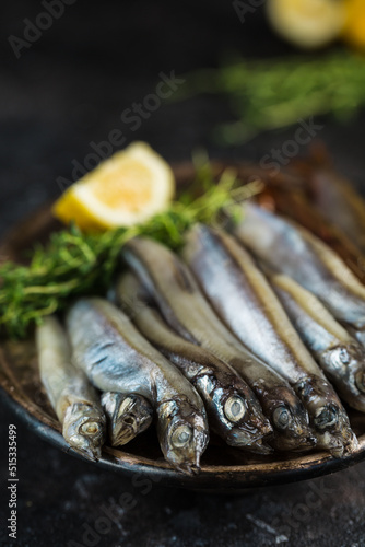 Pickled capelin with a slice of lemon and thyme on a metal plate on a dark background.