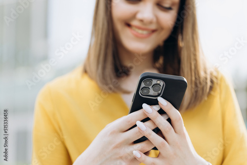 Joyful young attractive european business girl using mobile phone, smiling when reading sms, spending time outdoors. Urban people portraits