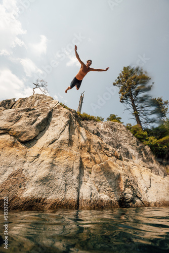 Man jumping from cliff into lake photo