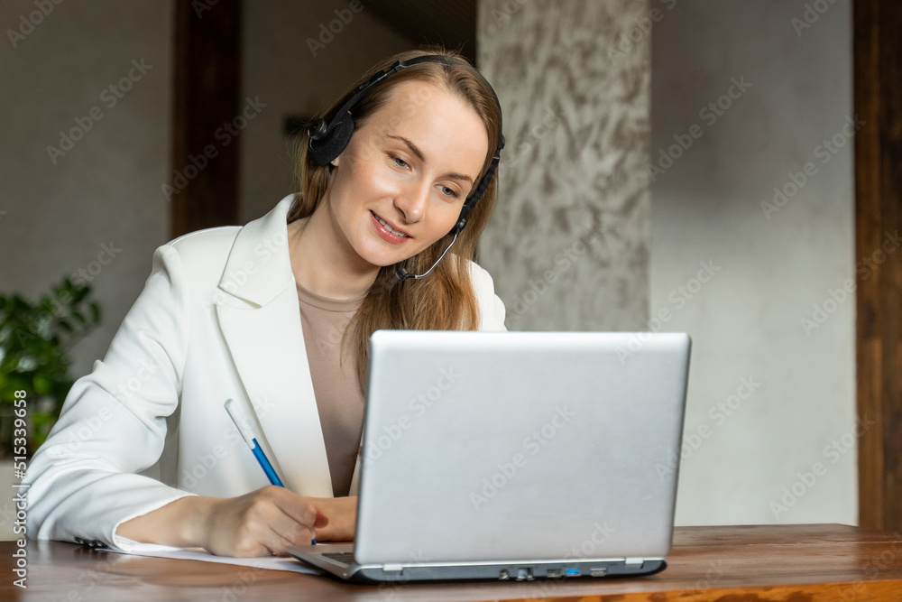 An attractive employee in a white jacket is sitting at her desk, holding a video conference with colleagues or clients. A woman with headphones, works as a call center operator. An attractive employee in a white jacket is sitting at her desk, holding a video conference with colleagues or clients. A woman with headphones, works as a call center operator.