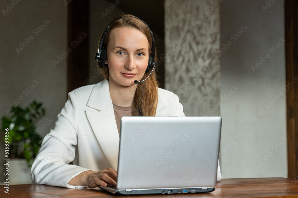 A confident young business woman in a white jacket and headphones discusses the details of the project with clients via video link. A female employee wearing headphones holds an online meeting with A confident young business woman in a white jacket and headphones discusses the details of the project with clients via video link. A female employee wearing headphones holds an online meeting with